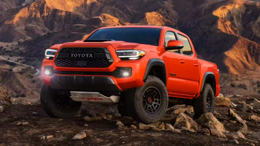 An orange 2023 Toyota Tacoma midsize pickup truck is parked off-road.