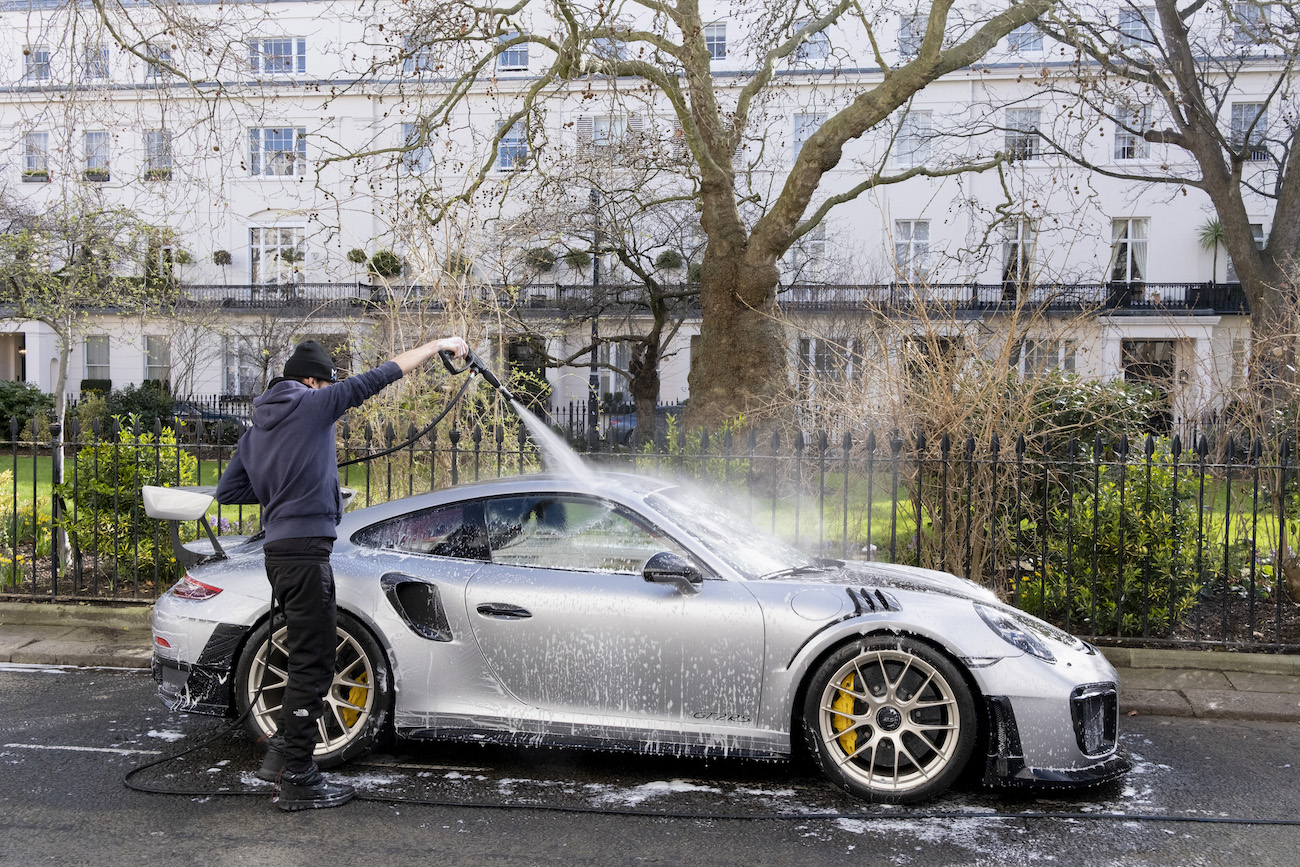 A car wash man cleans a luxury Porsche.