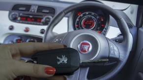 A woman holds a Peugeot car key as Fiat logo is seen behind.