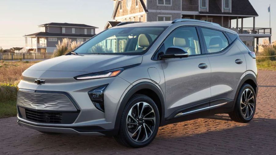 A silver-gray 2023 Chevy Bolt EUV compact electric SUV model parked outside of a home on a cobblestone road