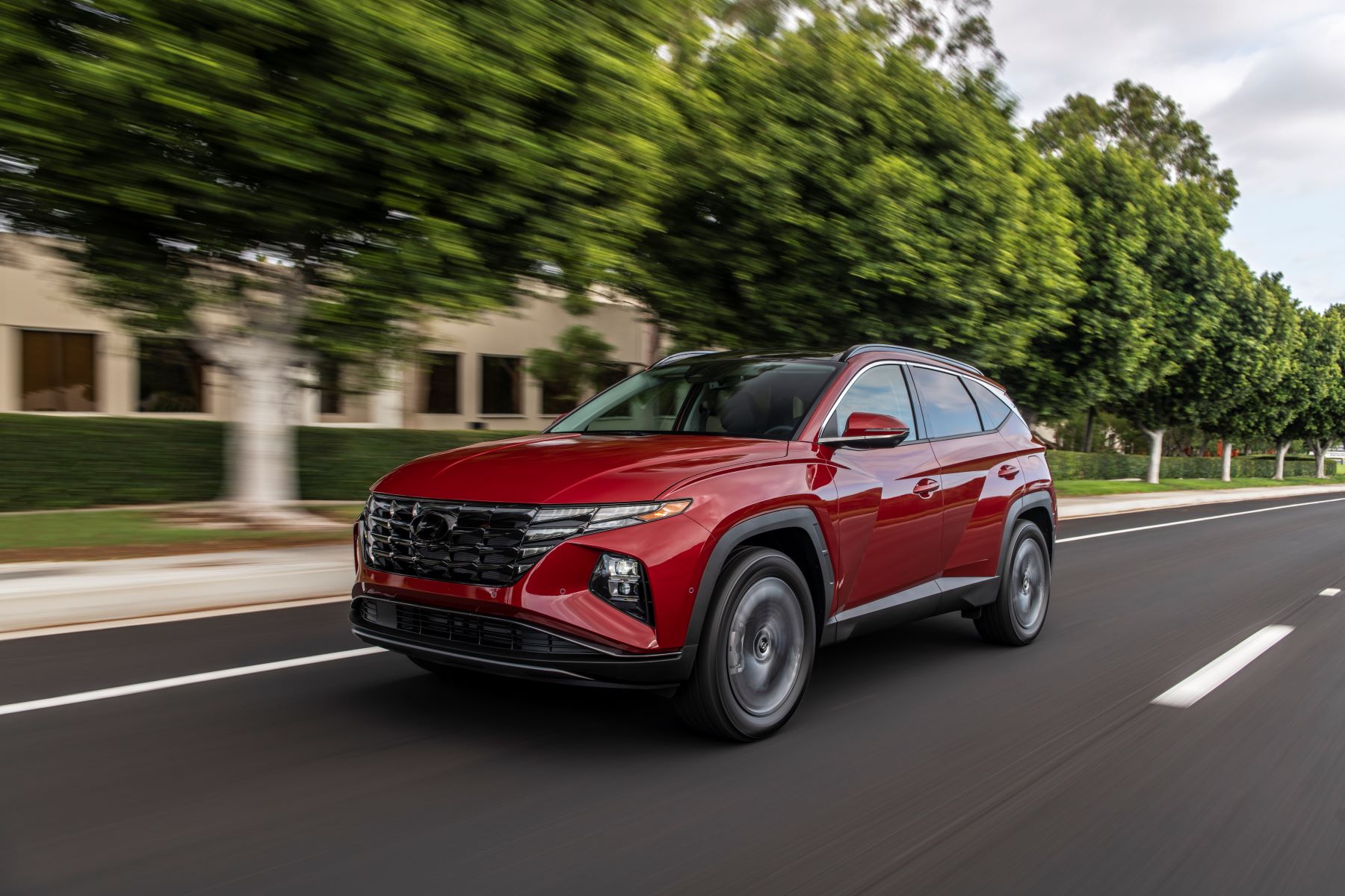 A red 2023 Hyundai Tucson compact SUV model driving down a suburb street lined by trees
