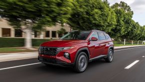 A red 2023 Hyundai Tucson compact SUV model driving down a suburb street lined by trees