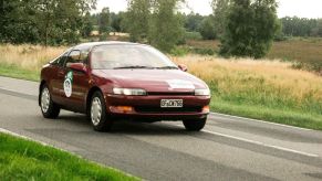 A red burgundy Toyota Sera hatchback coupe model driving on a country road