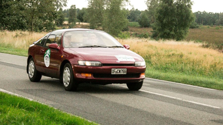 A red burgundy Toyota Sera hatchback coupe model driving on a country road