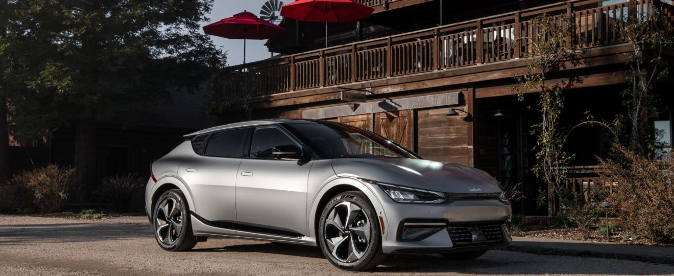 A silver-gray 2023 Kia EV6 compact electric SUV model parked on a gravel lot outside a wooden restaurant