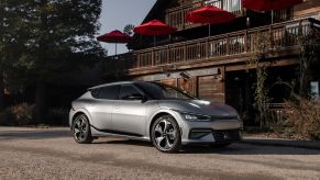 A silver-gray 2023 Kia EV6 compact electric SUV model parked on a gravel lot outside a wooden restaurant