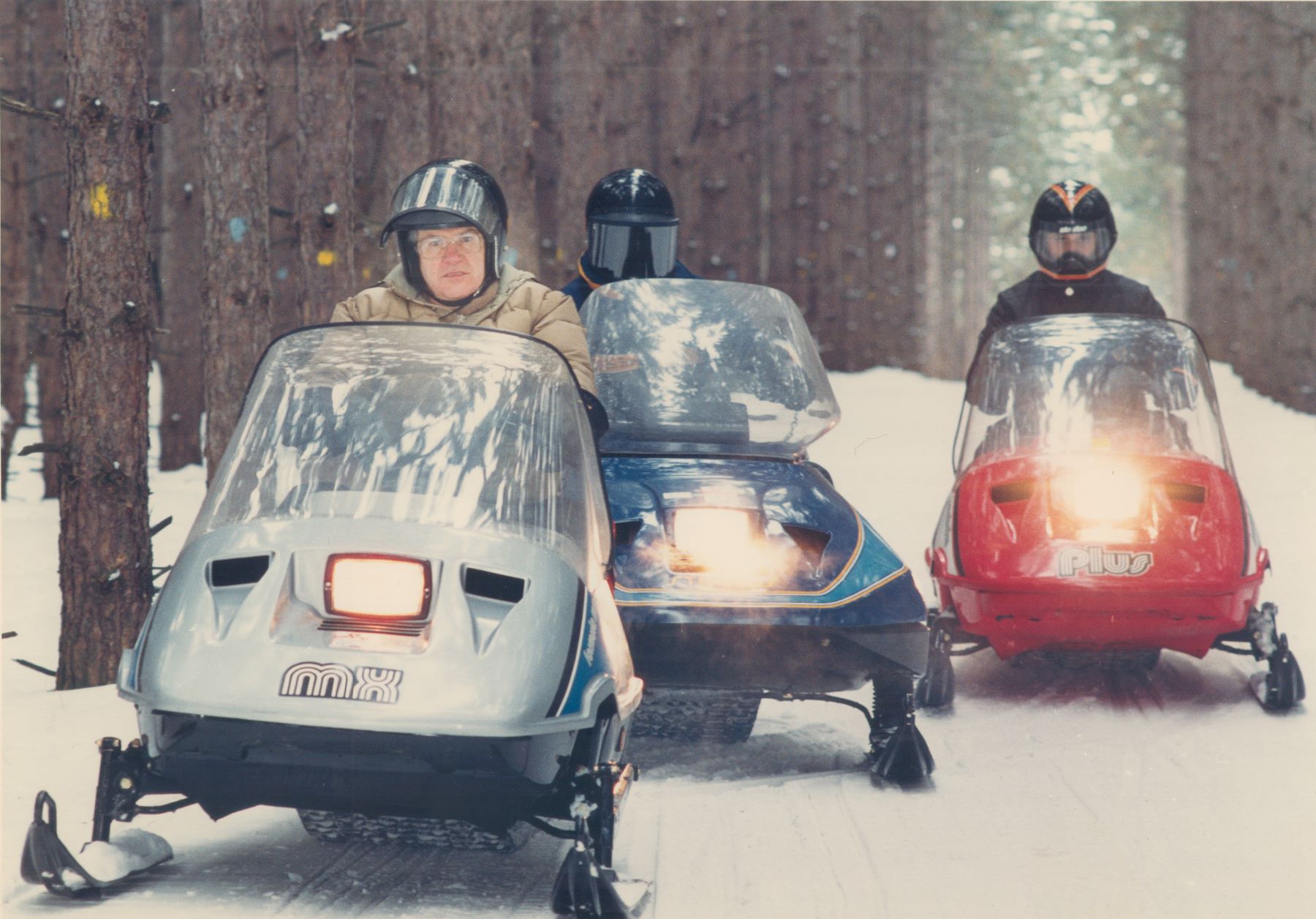 A group of snowmobilers practicing snowmobile safety by wearing helmets and traveling together in the winter snow