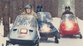 A group of snowmobilers practicing snowmobile safety by wearing helmets and traveling together in the winter snow