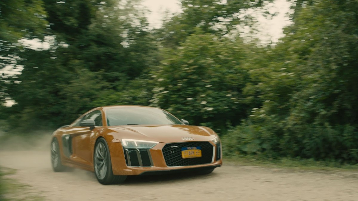 An Audi R8 driving on a dirt road by some trees