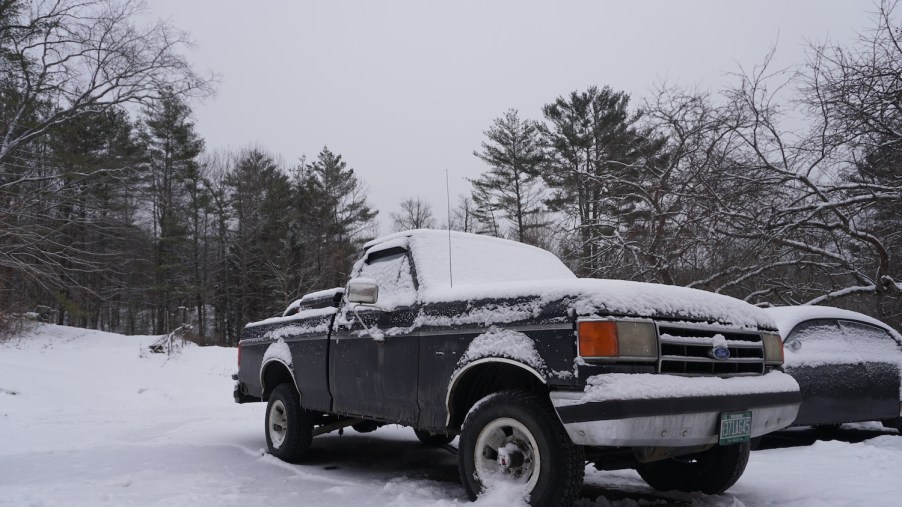 A black Ford F-150 pickup truck covered in snow, has a larger engine with more oil that might have problems in cold weather starting.