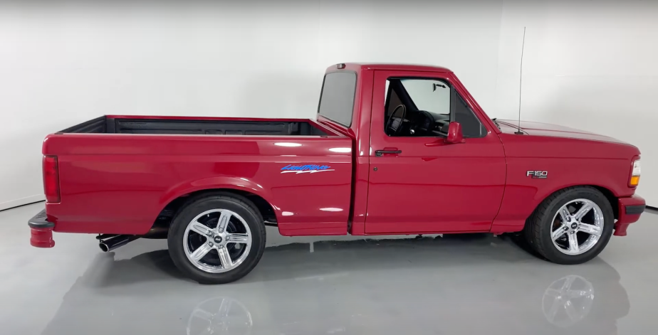 Side shot of a 1994 Red Ford  F-150 SVT Lightning muscle truck parked in a showroom, a white wall visible in the background.
