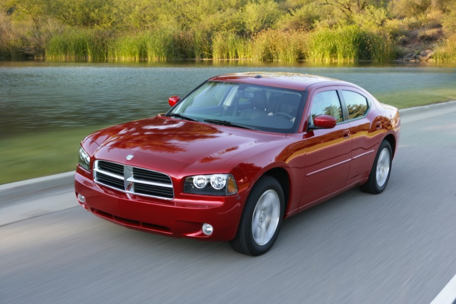Promo photo of a red Dodge Charger driving up a country road, a lake and plants visible in the background.