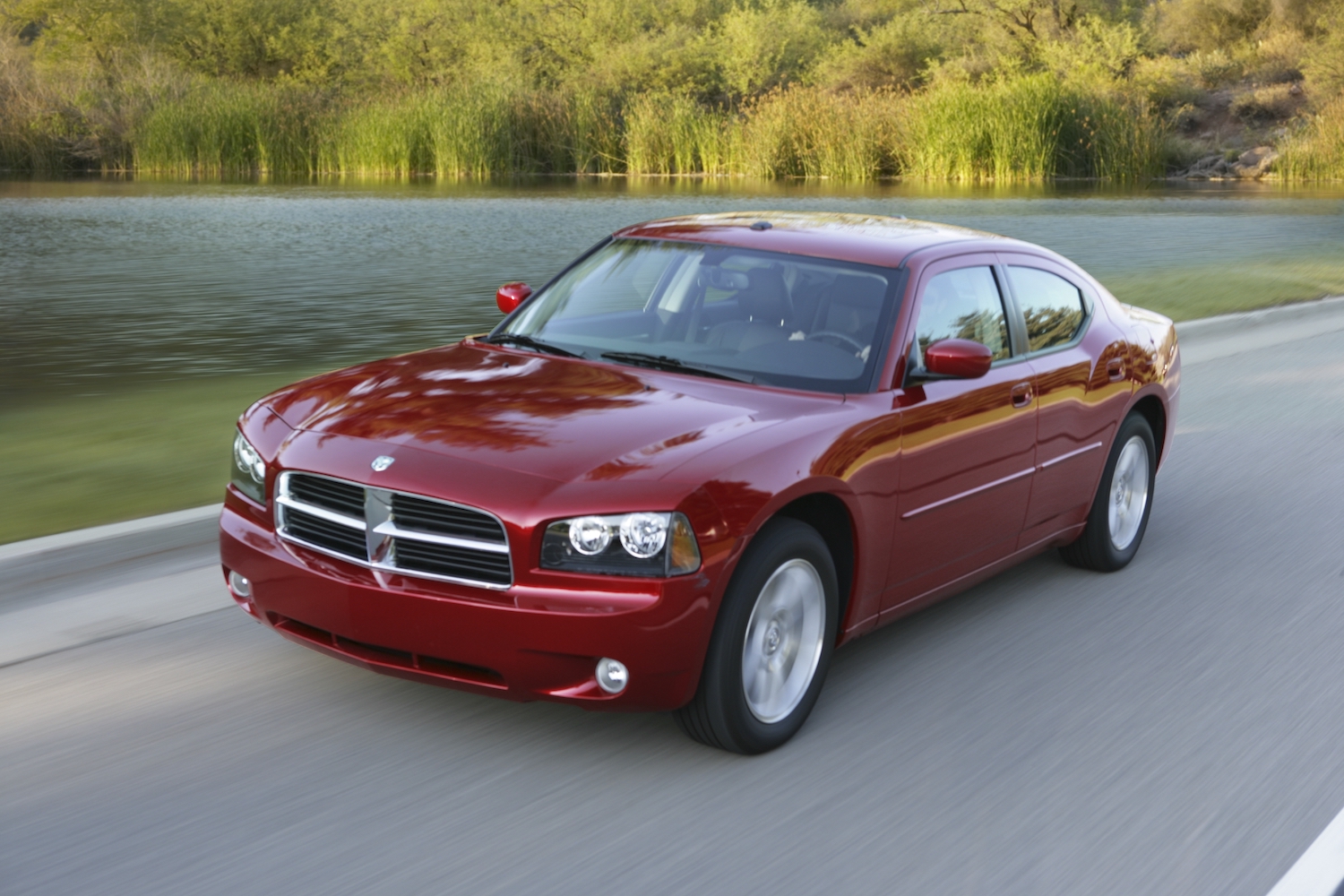 Red 2010 Dodge charger driving along a remote road, a pond visible in the background.