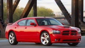 Red 2010 Dodge Charger sedan parked on a bridge, in front of rusted iron uprights.