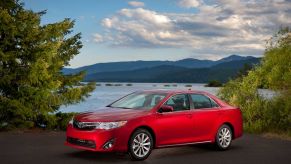 A red 2012-2014 Toyota Camry SE generation midsize sedan model parked near forest trees and the sea