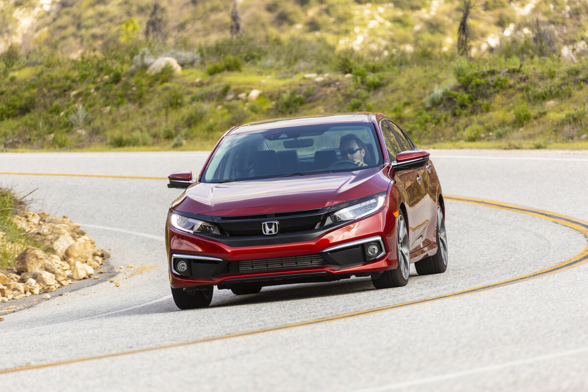 A red 2019 Honda Civic Sedan takes a corner on a country road.