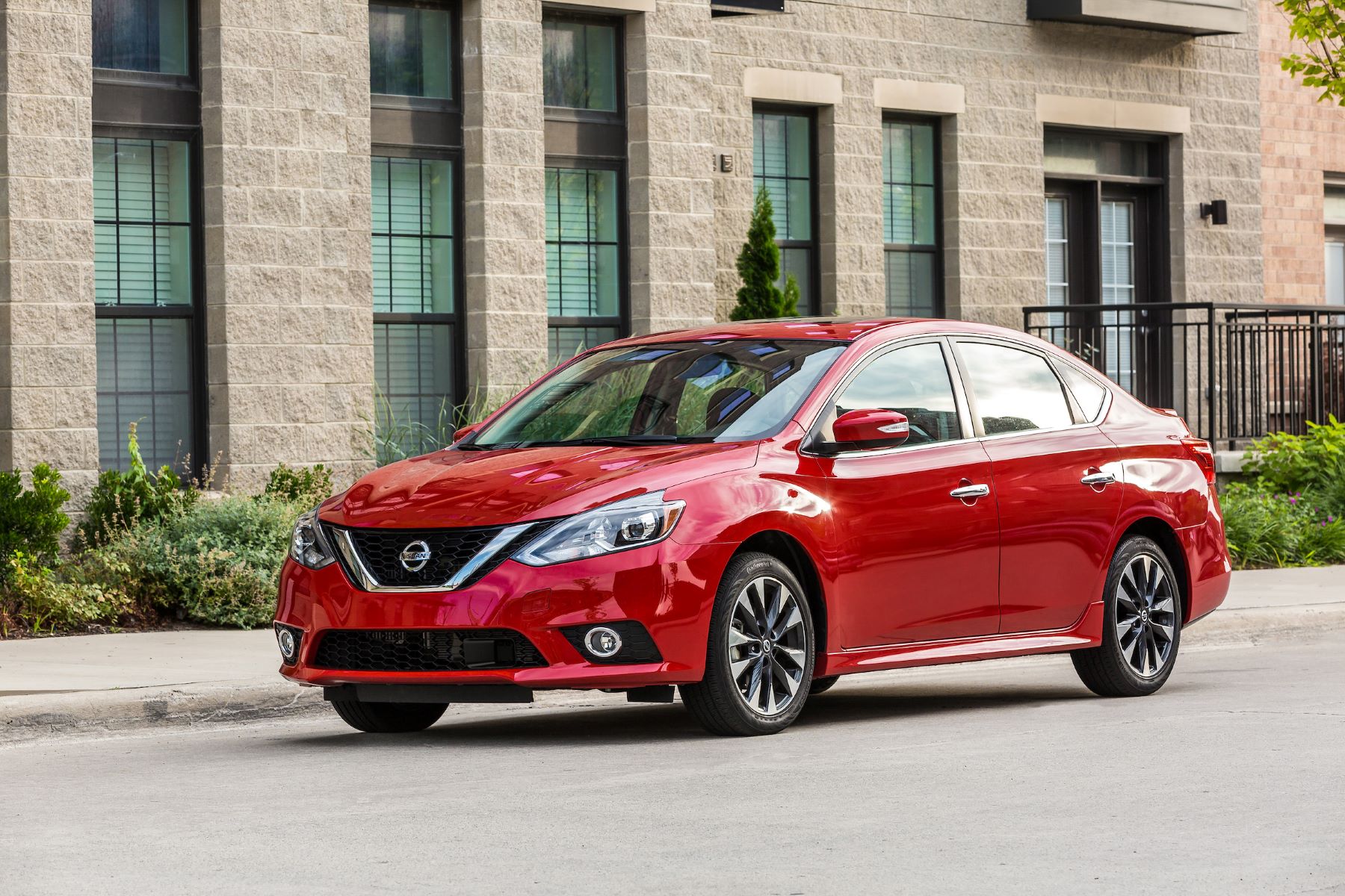 A red 2019 Nissan Sentra SR Turbo compact sedan parked outside a gray brick building