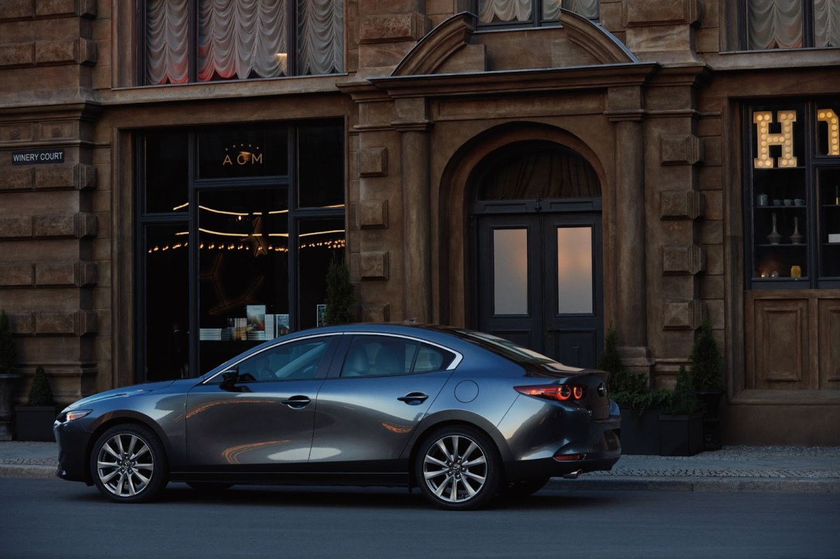 A gray Mazda3 sedan parked in front of a city building