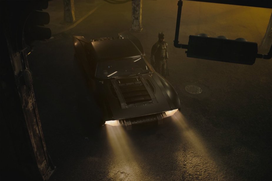 Bird's eye view of the 2022 Batmobile parked in Gotham City with batman standing next to it.