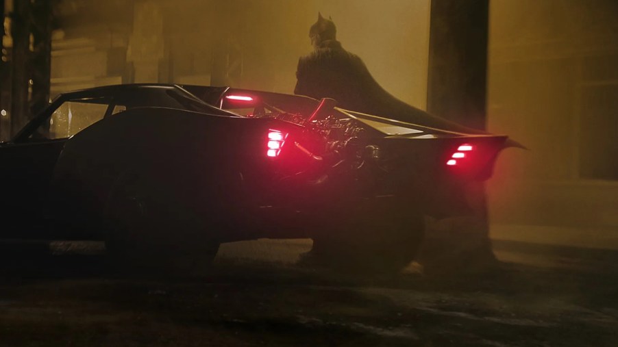 Robert Pattinson's Batman standing behind the 2022 Batmobile based on a 1969 Dodge Charger.