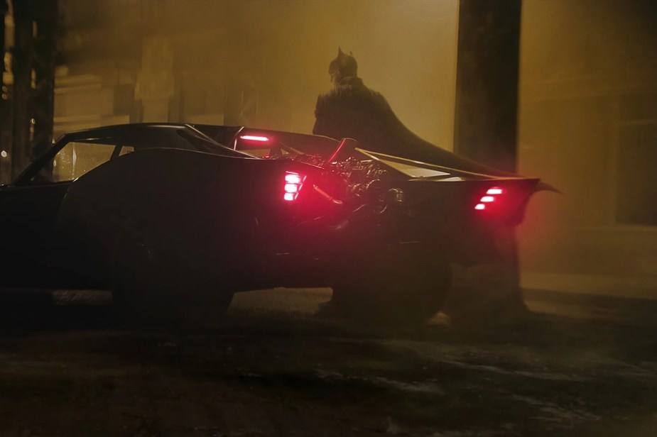 Actor Robert Pattinson standing behind the 2022 Batmobile for a publicity shot of his superhero movie.