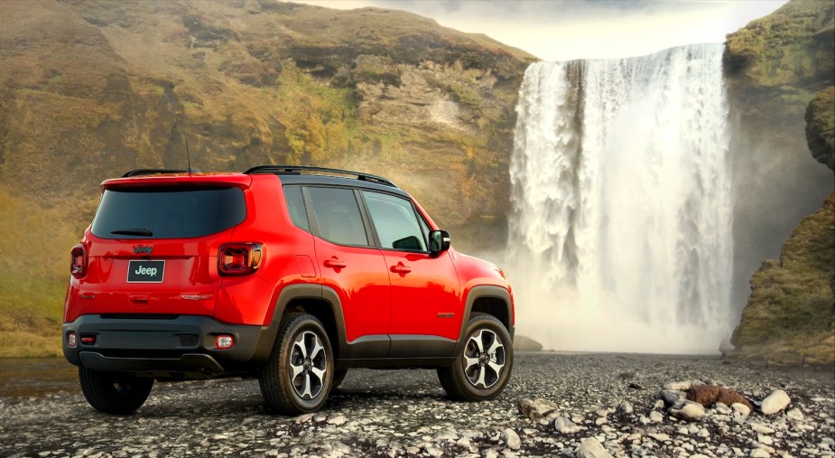 Promo photo of a red Jeep Renegade crossover parked off road, in front of a waterfall.