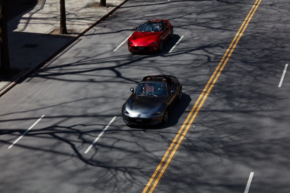 Two Mazda Miata models on a multi-lane city road