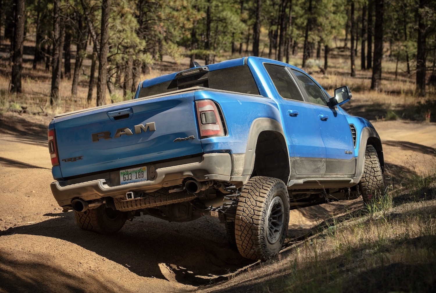 A blue Ram 1500 TRX parked on a dirt road, trees visible in the background.