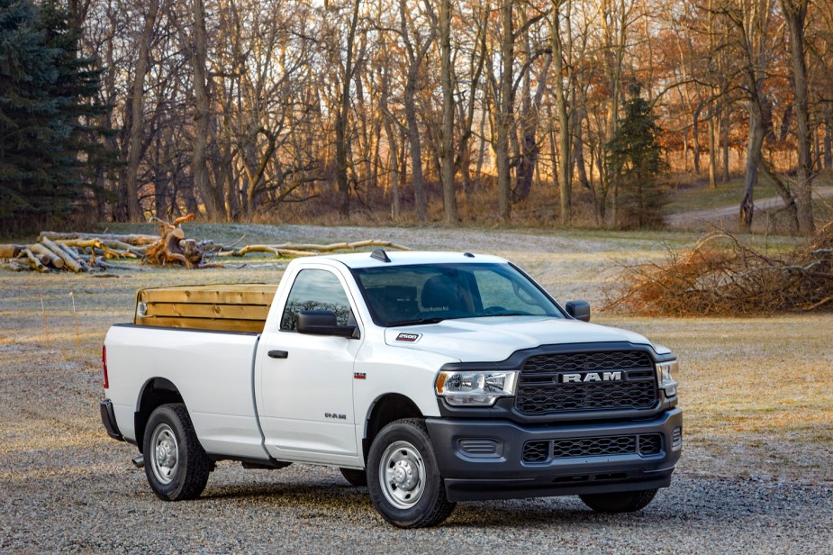 A Ram 2500 Tradesman work truck with a bed full of lumber is parked in front of a row of trees.