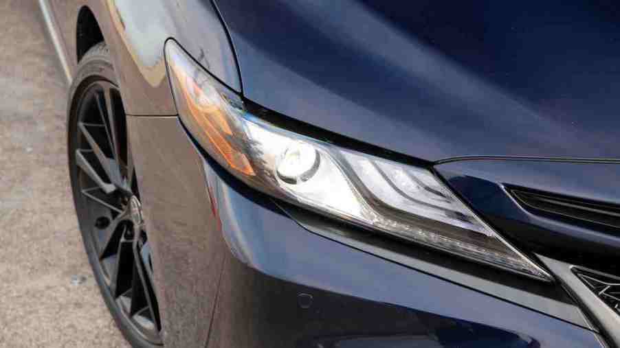 The headlight of a black Toyota Camry, which is a part of one of the most reliable car brands.