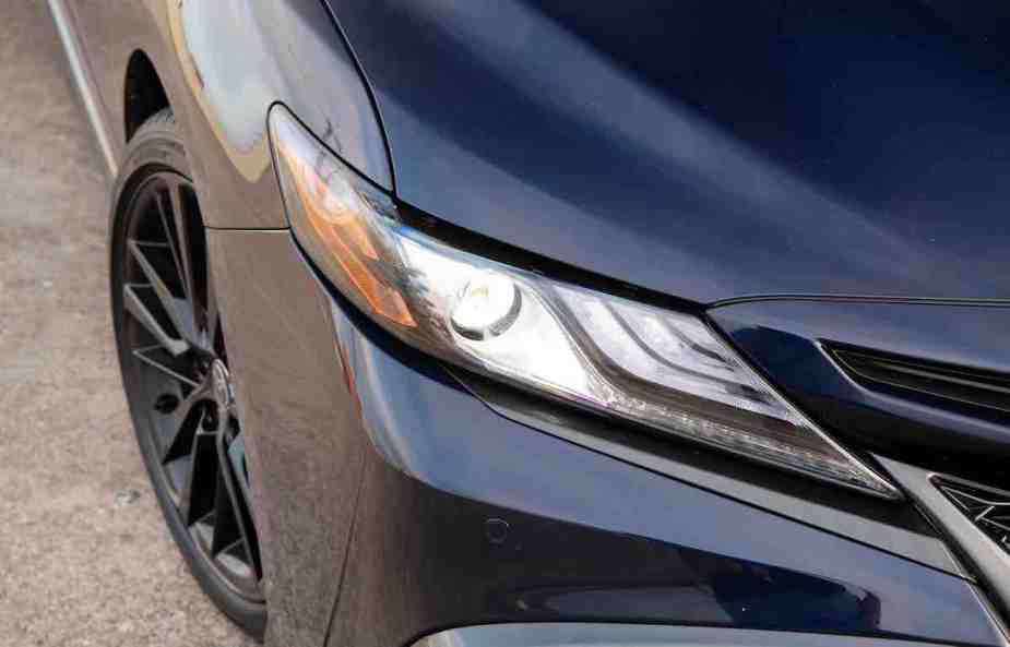 The headlight of a black Toyota Camry, which is a part of one of the most reliable car brands. 