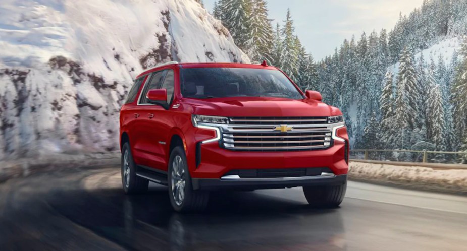 A red 2023 Chevrolet Suburban full-size SUV is driving on the road.