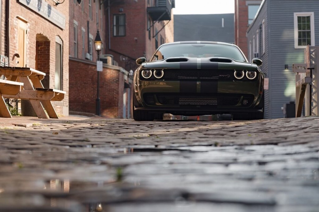 A 2023 Dodge Challenger SRT Hellcat, like the R/T Scat Pack, shows off its retro lights and wide stance on a cobblestone road. 