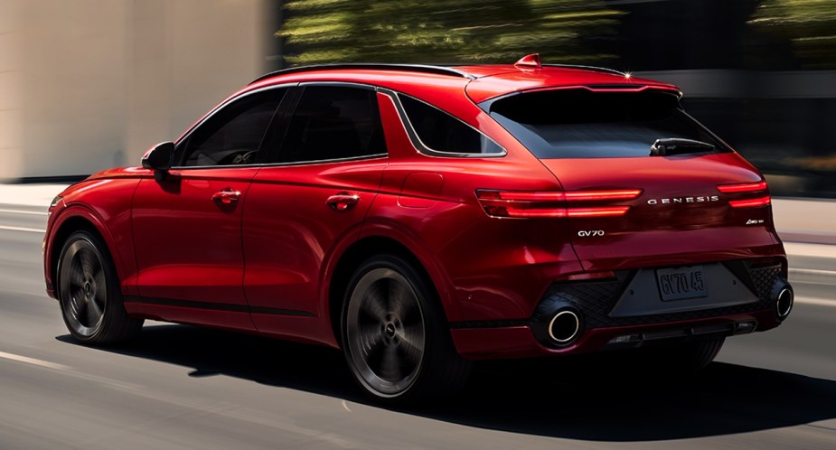 The back of a red 2023 Genesis GV70 small luxury SUV is driving on the road. 