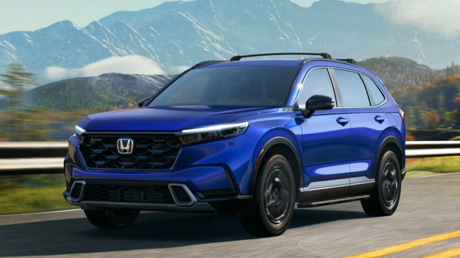 A blue 2023 Honda CR-V LX, the entry level trim, is driving on the road.