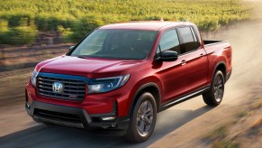A red 2023 Honda Ridgeline midsize pickup truck is driving off-road.
