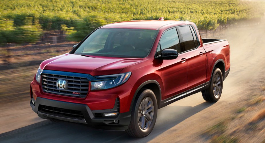 A red 2023 Honda Ridgeline midsize pickup truck is driving off-road. 