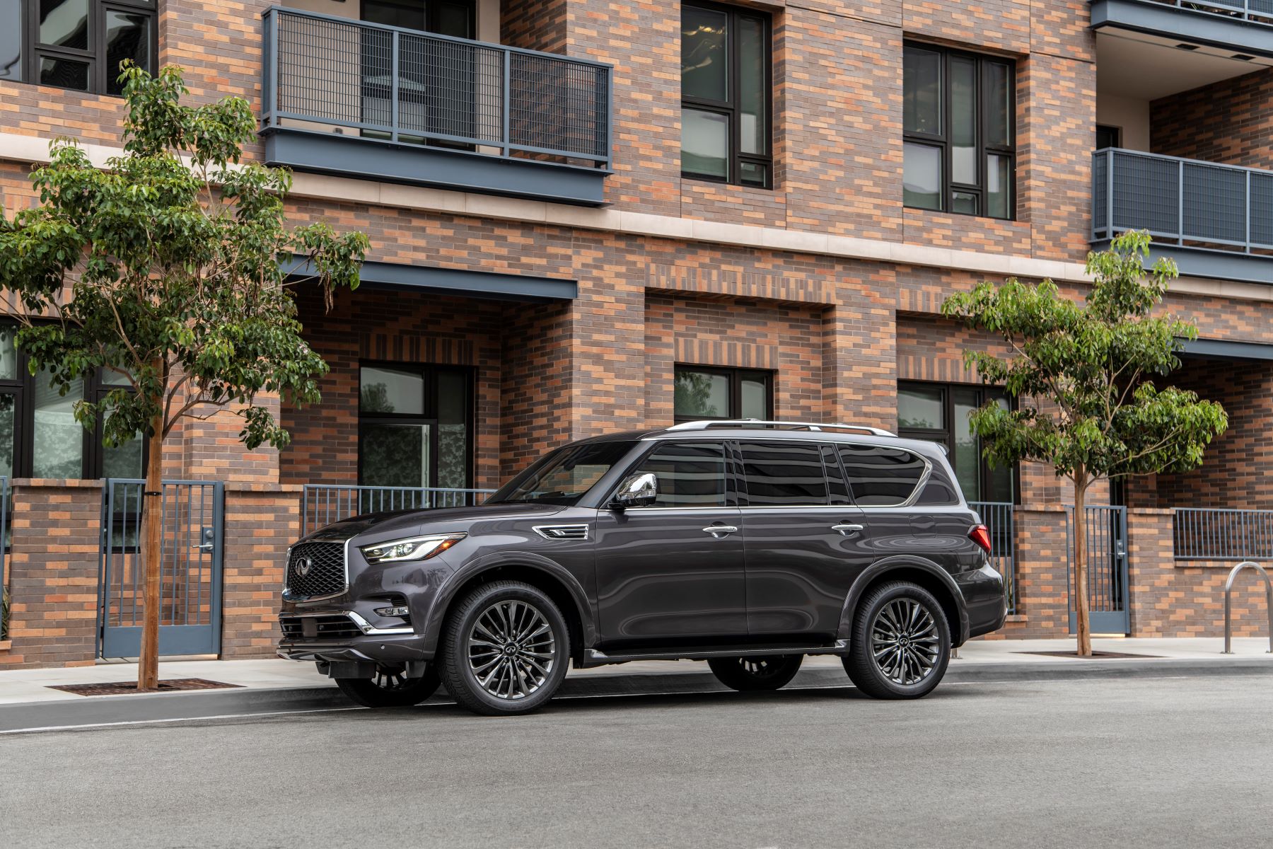 A dark gray 2023 Infiniti QX80 full-size luxury SUV model parked outside a brick apartment building