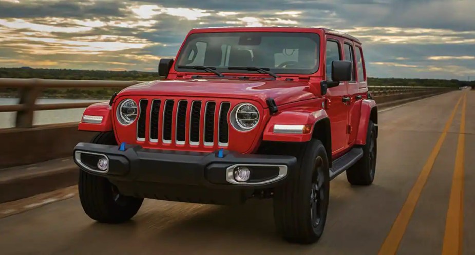 A red 2023 Jeep Wrangler small SUV is driving on the road. 