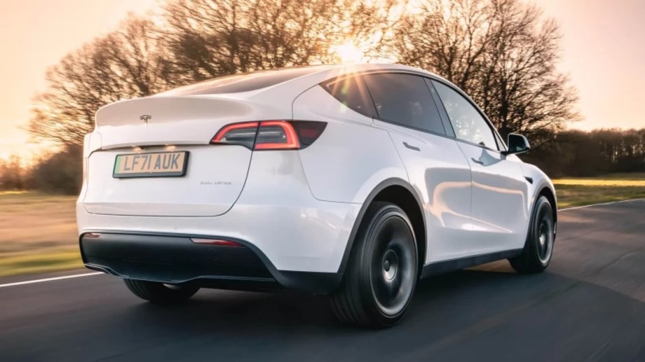 Rear View of a White 2023 Tesla Model Y small electric SUV with a sunset in the background.