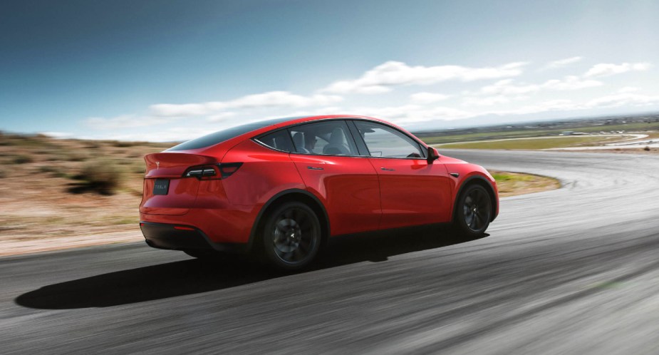 A red Tesla Model Y small electric SUV is driving on the road. 