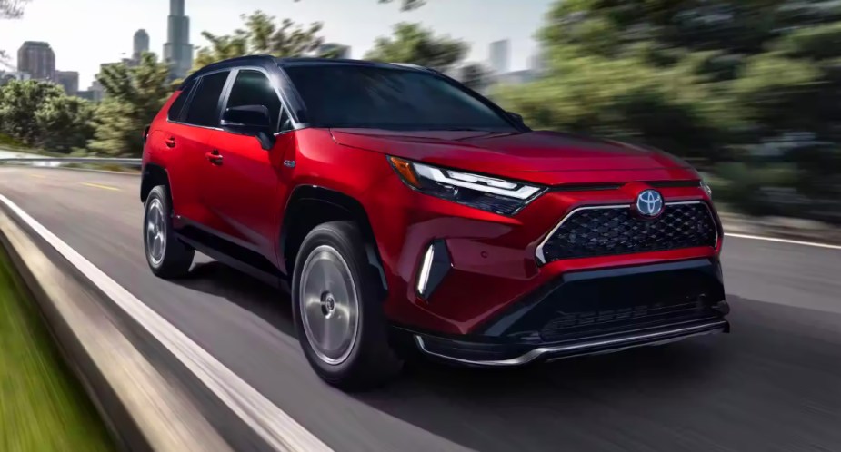A red 2023 Toyota RAV4 Prime small plug-in hybrid SUV is driving on the road. 