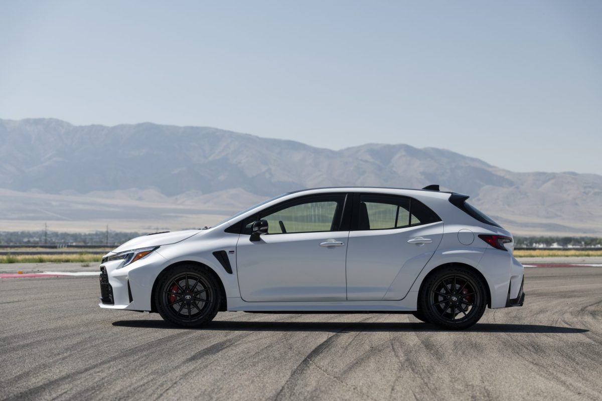 A white GR Corolla in side profile, parked on a race track with a mountainous backdrop.