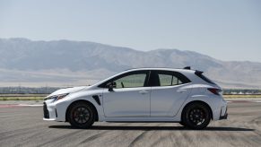 Side profile of a GR Corolla in white, parked on a race track in front of some mountains