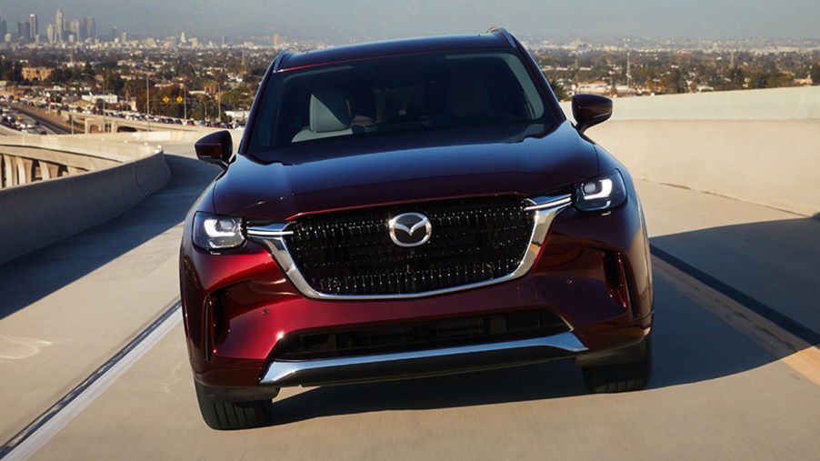 A red 2024 Mazda CX-90 midsize SUV is driving.