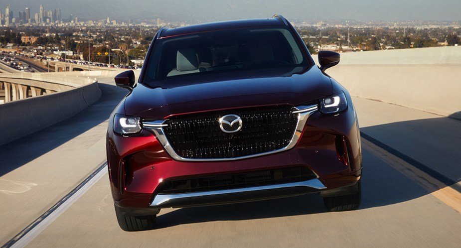 A red 2024 Mazda CX-90 midsize SUV is driving on the road. 