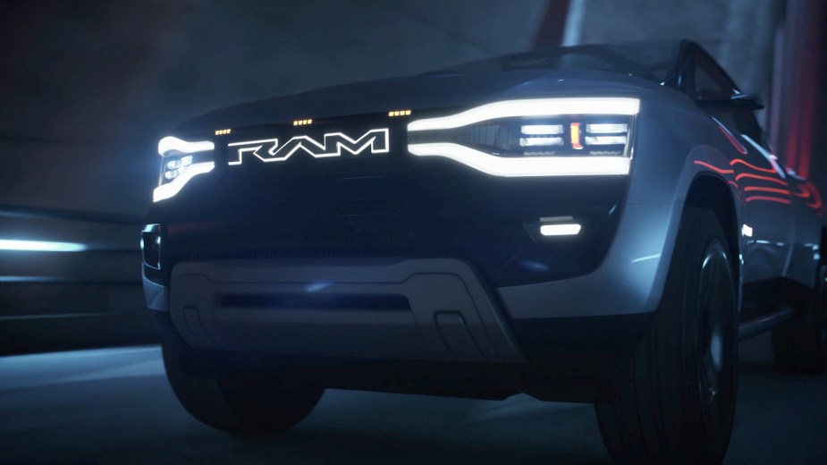 Closeup of the grille of Ram's 1500 Revolution electric truck prototype with its logo and headlight LEDs illuminated while driving under a bridge at night.