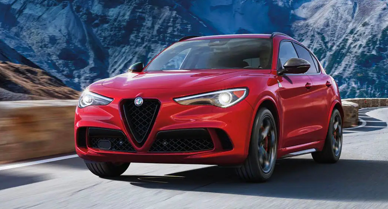 A red 2023 Alfa Romeo Stelvio small luxury SUV is driving on the road.