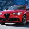 A red 2023 Alfa Romeo Stelvio small luxury SUV is driving on the road.