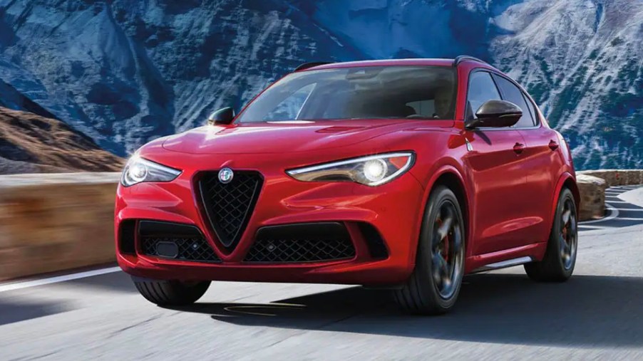 A red 2023 Alfa Romeo Stelvio small luxury SUV is driving on the road.